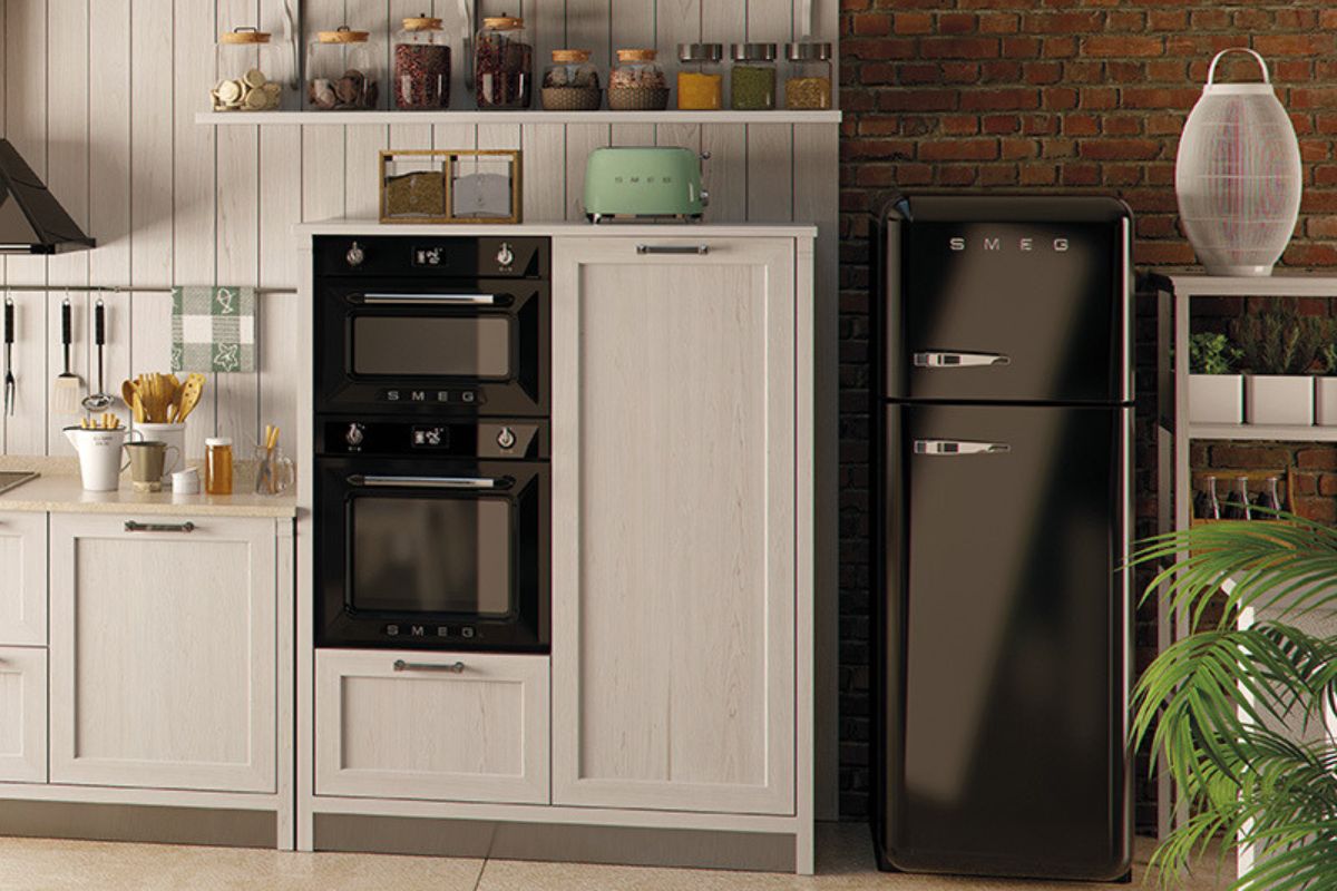 Black SMEG built-in ovens and a freestanding refrigerator in a kitchen with exposed brick