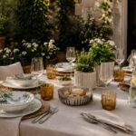 tavola estiva apparecchiata in giardino con piatti eleganti e bicchieri colorati