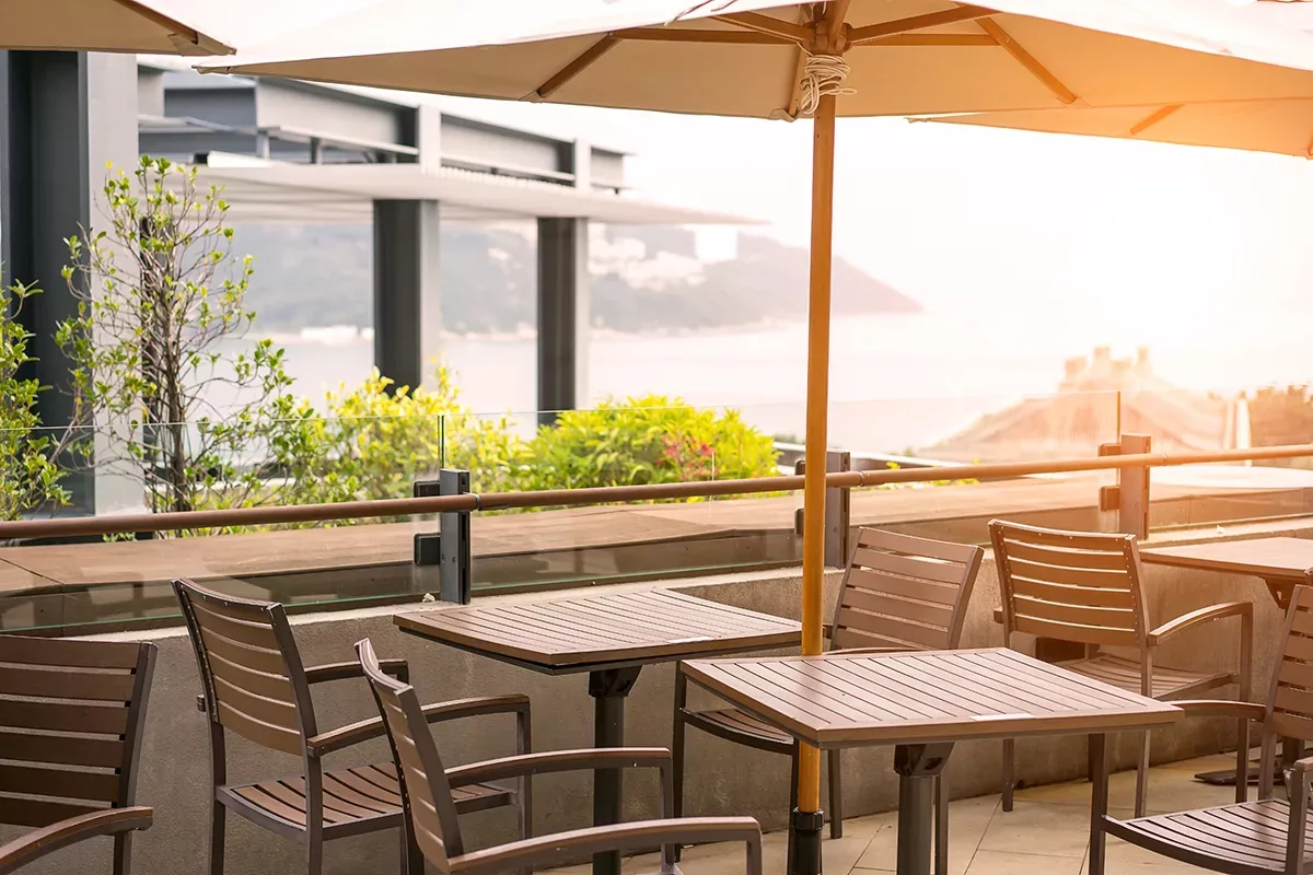 Rooftop di ristorante con tavoli in legno e vista sul mare al tramonto