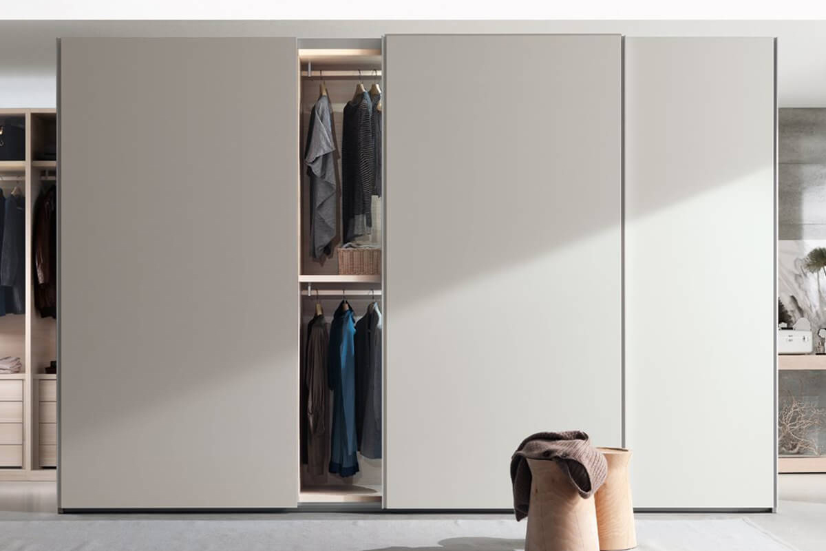 Armadio moderno con ante scorrevoli color avorio e interno illuminato con abiti ordinati.