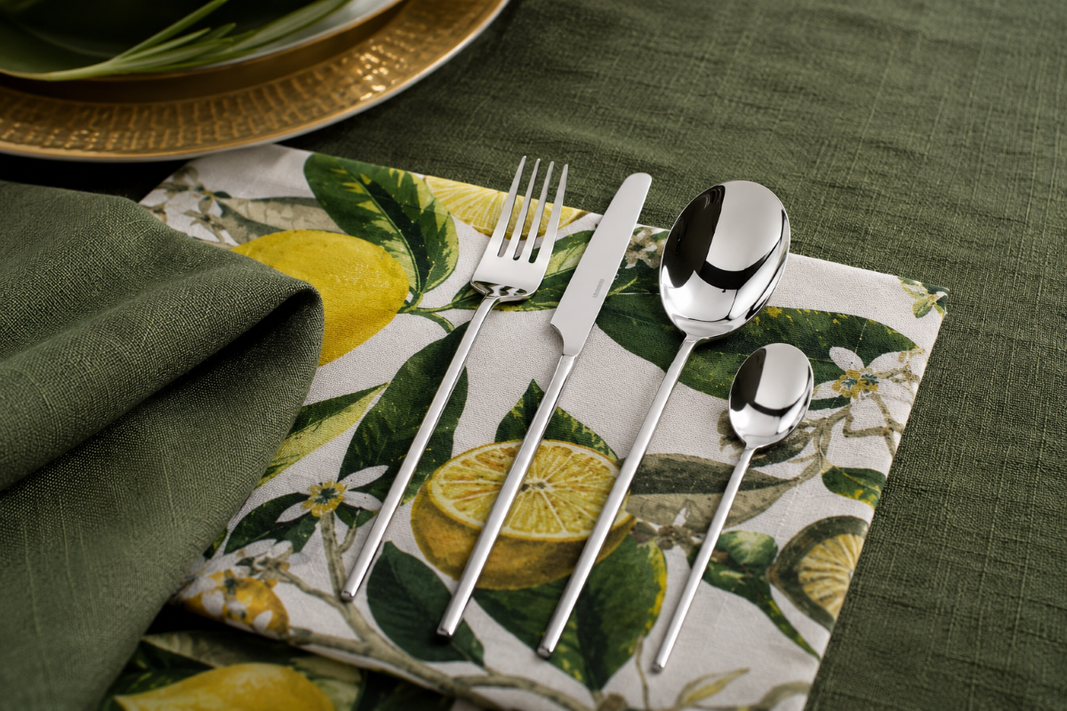 Tovaglia in lino verde con posate di design e dettaglio decorativo botanico.