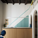 Cucina di Casa Iolascon a Napoli con isola in rovere, scala verde acqua e soffitto ligneo restaurato