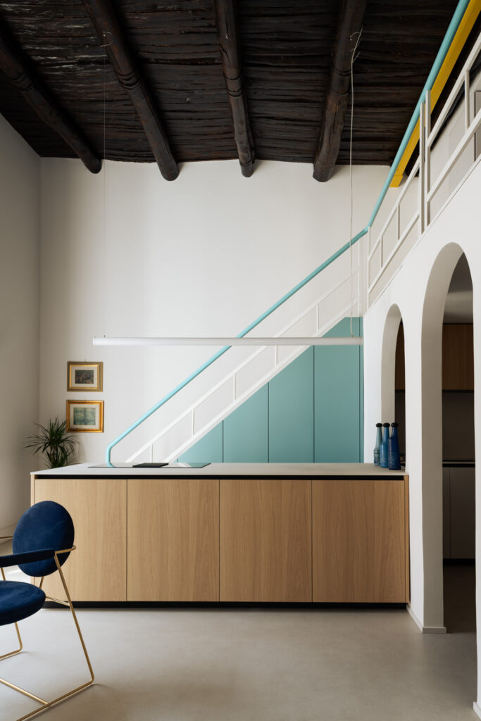 Cucina di Casa Iolascon a Napoli con isola in rovere, scala verde acqua e soffitto ligneo restaurato