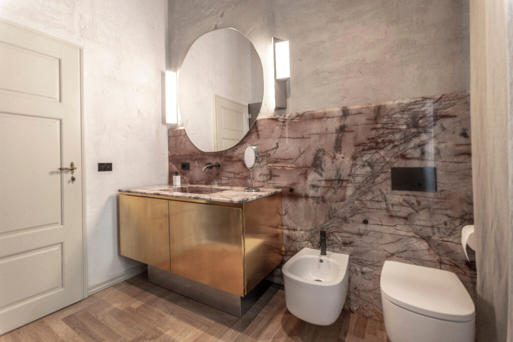 Bagno con finiture dorate e marmo dalle venature rosate a Casa Trezza