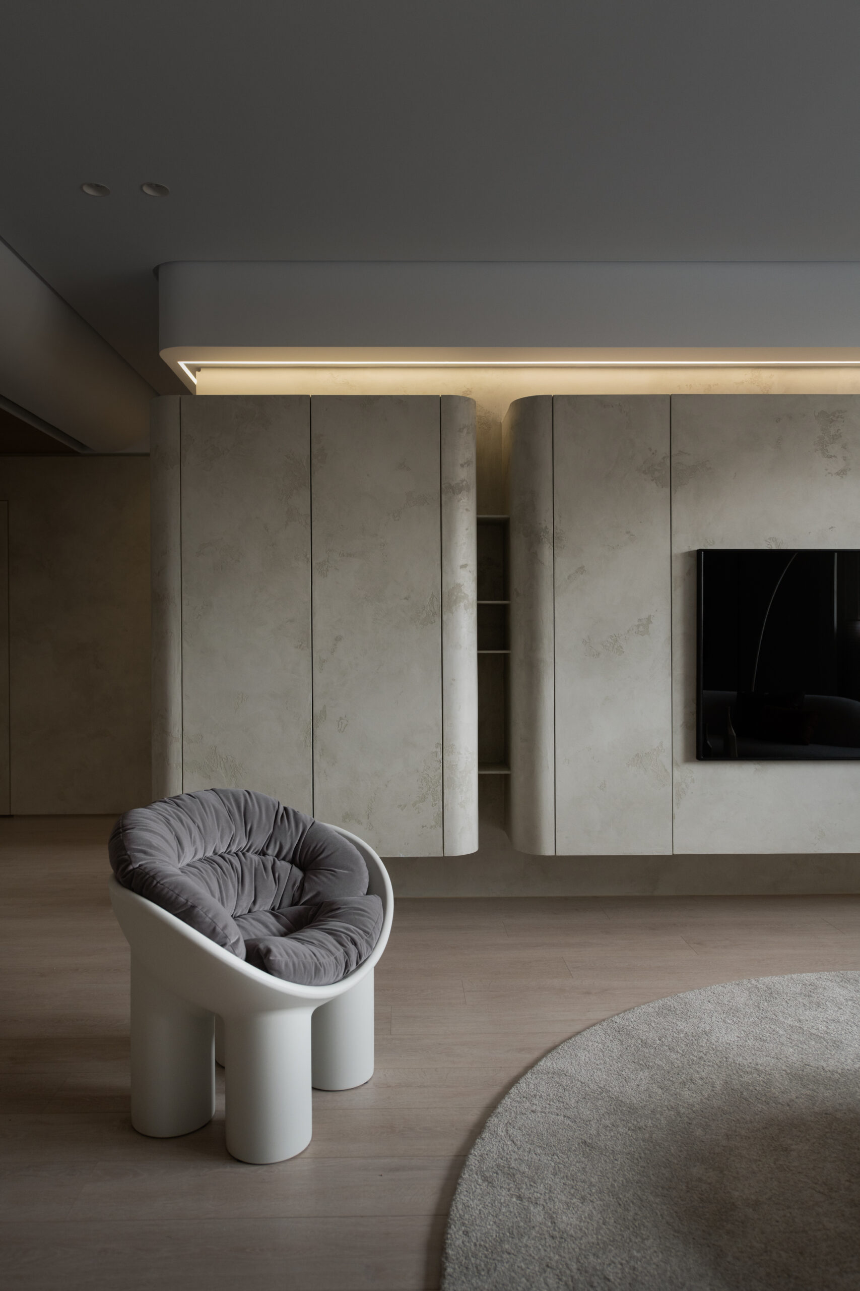 Grey-beige textured wall and built-in units above a pale timber floor, with a grey cushioned chair