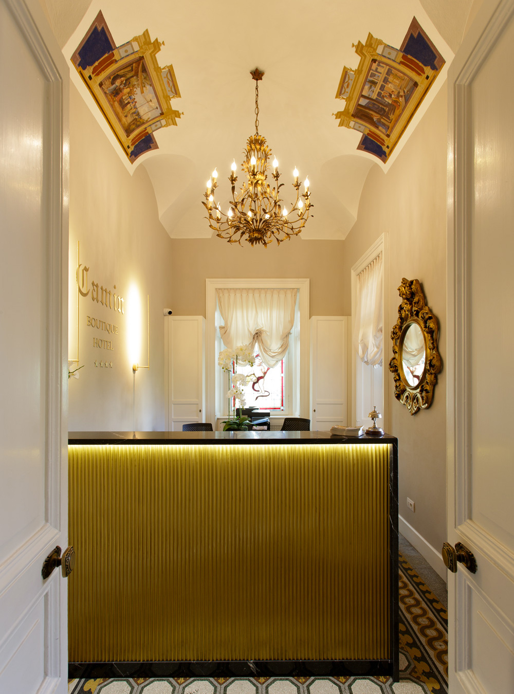 Camin Boutique Hotel entrance with a gold-toned reception desk, mirror and frescoed ceiling.