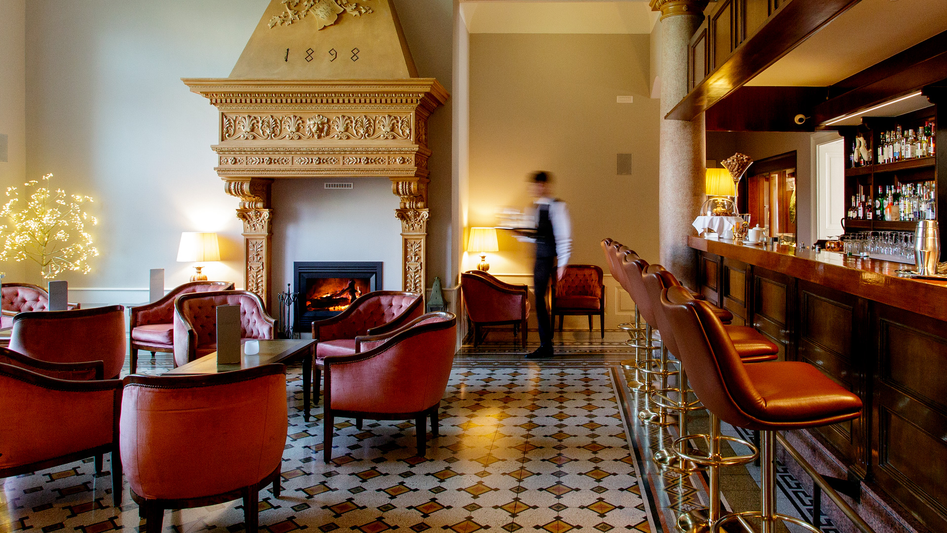 Camin Boutique Hotel salon in Luino with an ornate fireplace, burgundy armchairs and a timber bar.