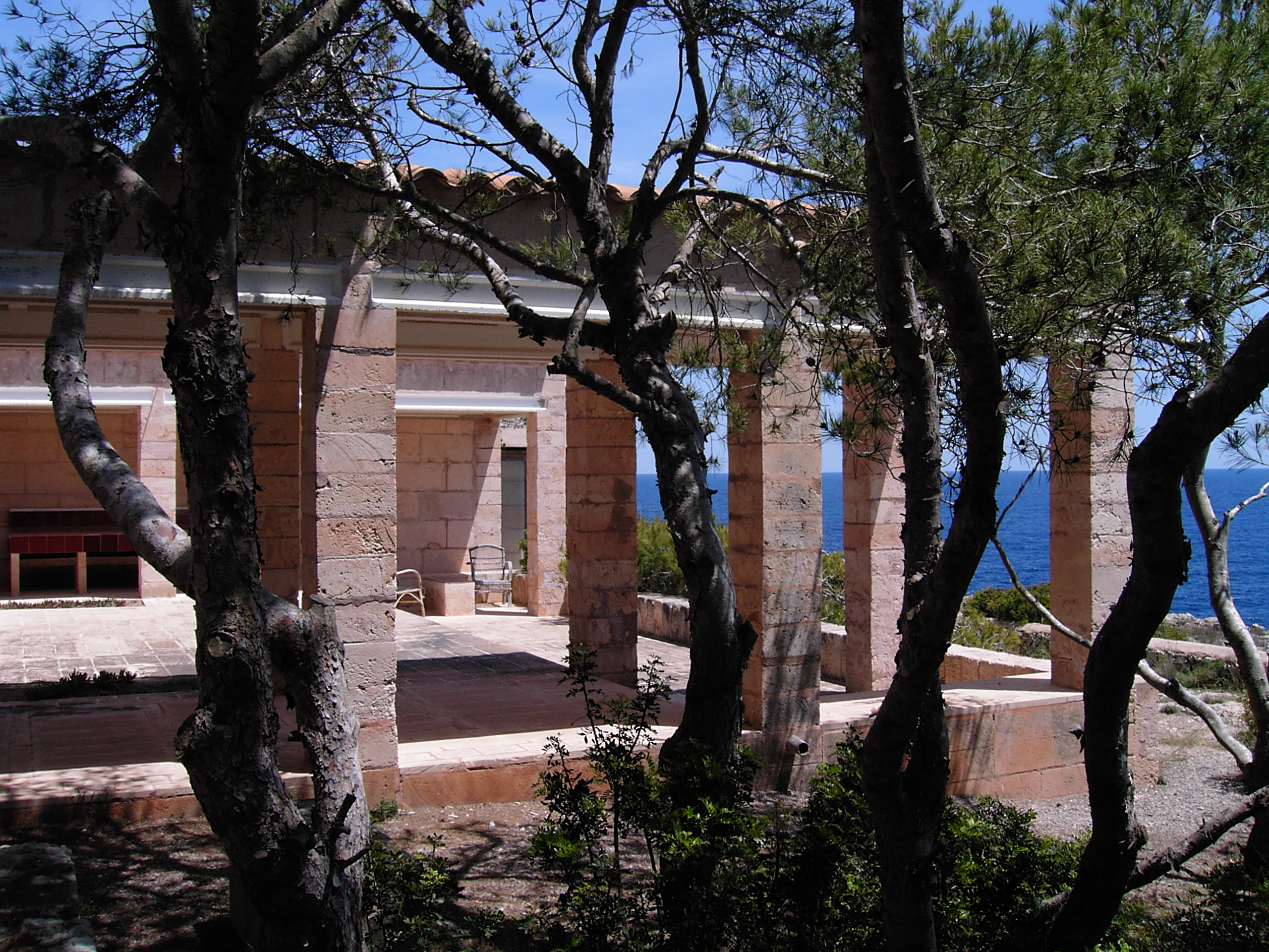 Portico in pietra di Can Lis tra i pini, con il mare visibile oltre le colonne