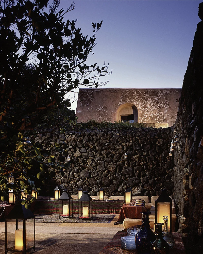 Dammuso illuminato di sera dietro un muro di pietra lavica a Pantelleria