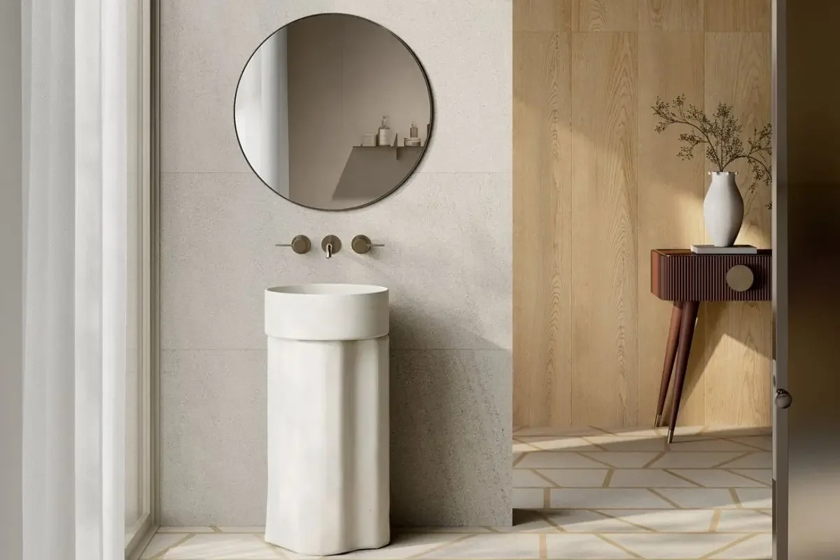 Lavabo bianco a colonna sotto uno specchio rotondo in un bagno neutro