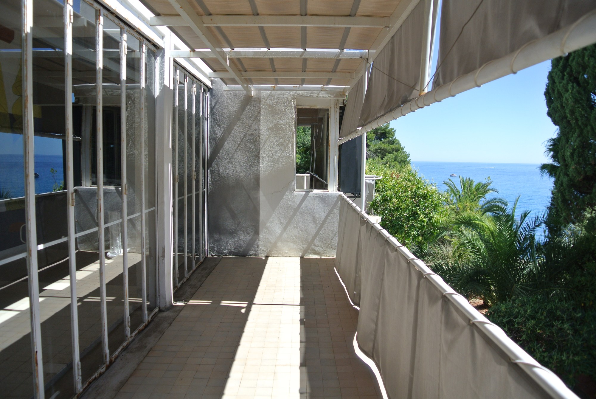 Balcone di E-1027 con finestre a libro, tenda ombreggiante e vista sul Mediterraneo tra i pini