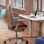 Sedia da ufficio Fern di Haworth accanto a una scrivania regolabile in un loft con pavimento in legno e mattoni a vista