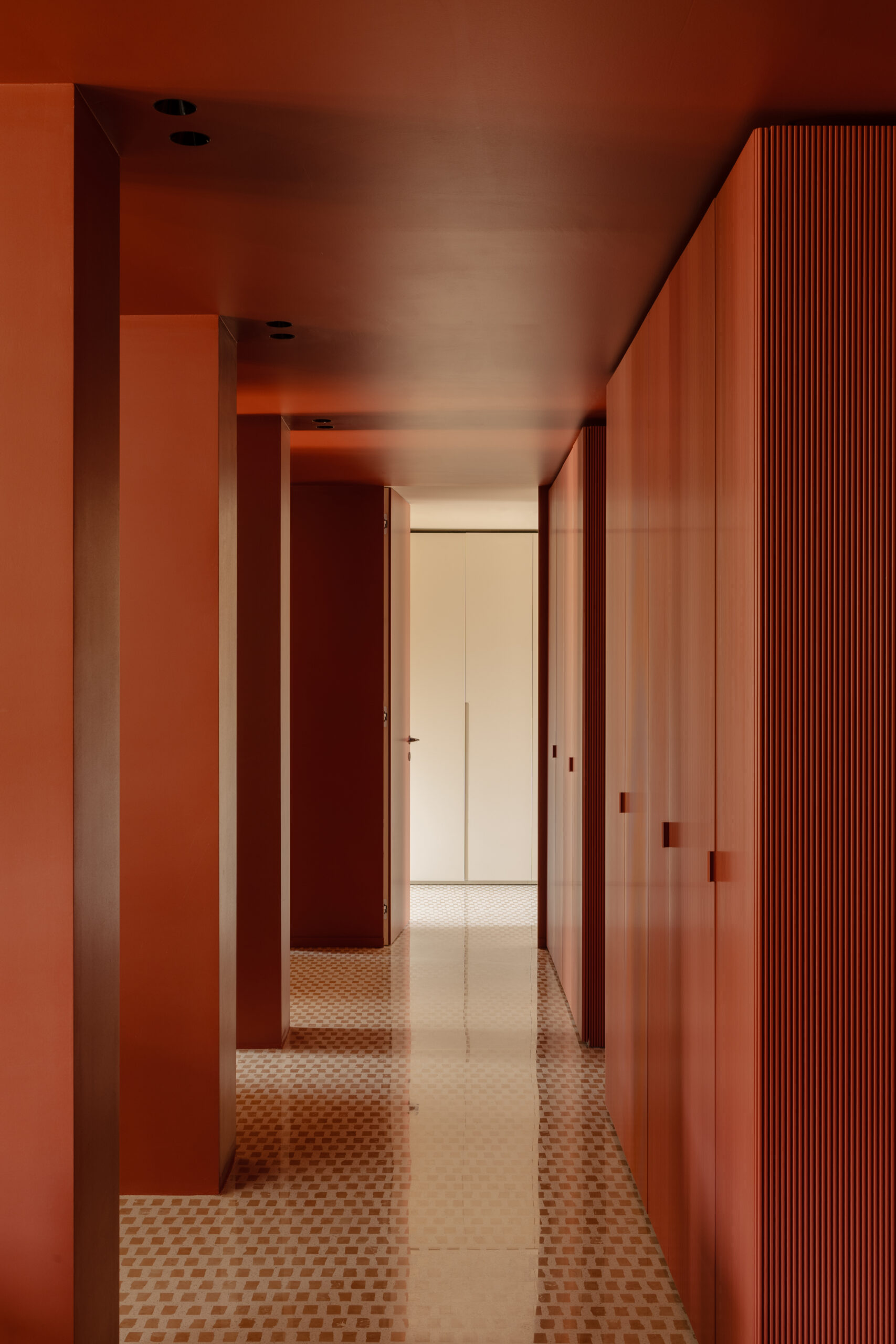 Corridoio terracotta con pilastri su un lato, armadi a tutta altezza sull'altro e pavimento a piccoli quadrati.