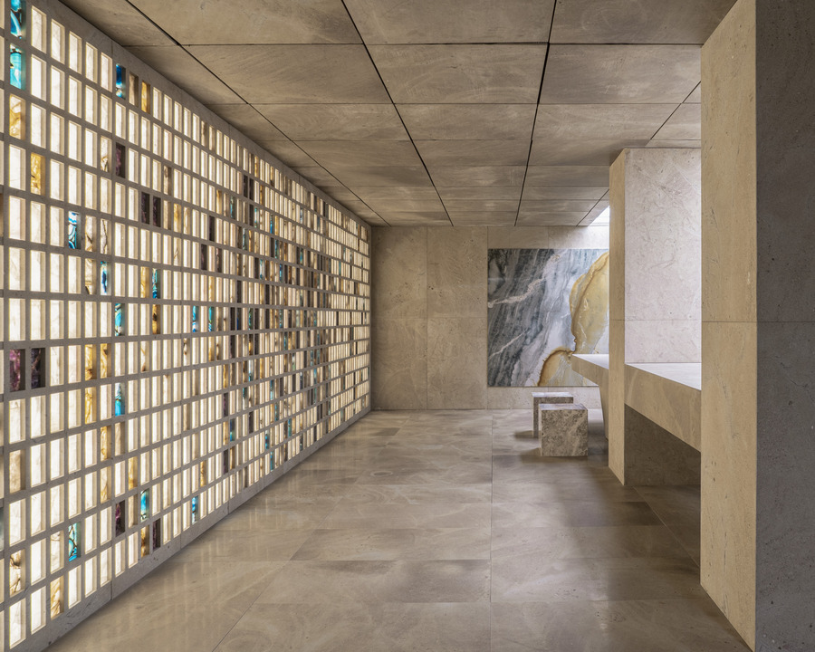Ambiente in pietra con parete a griglia di tessere luminose, soffitto a grandi lastre, bancone sulla destra e parete venata sul fondo.