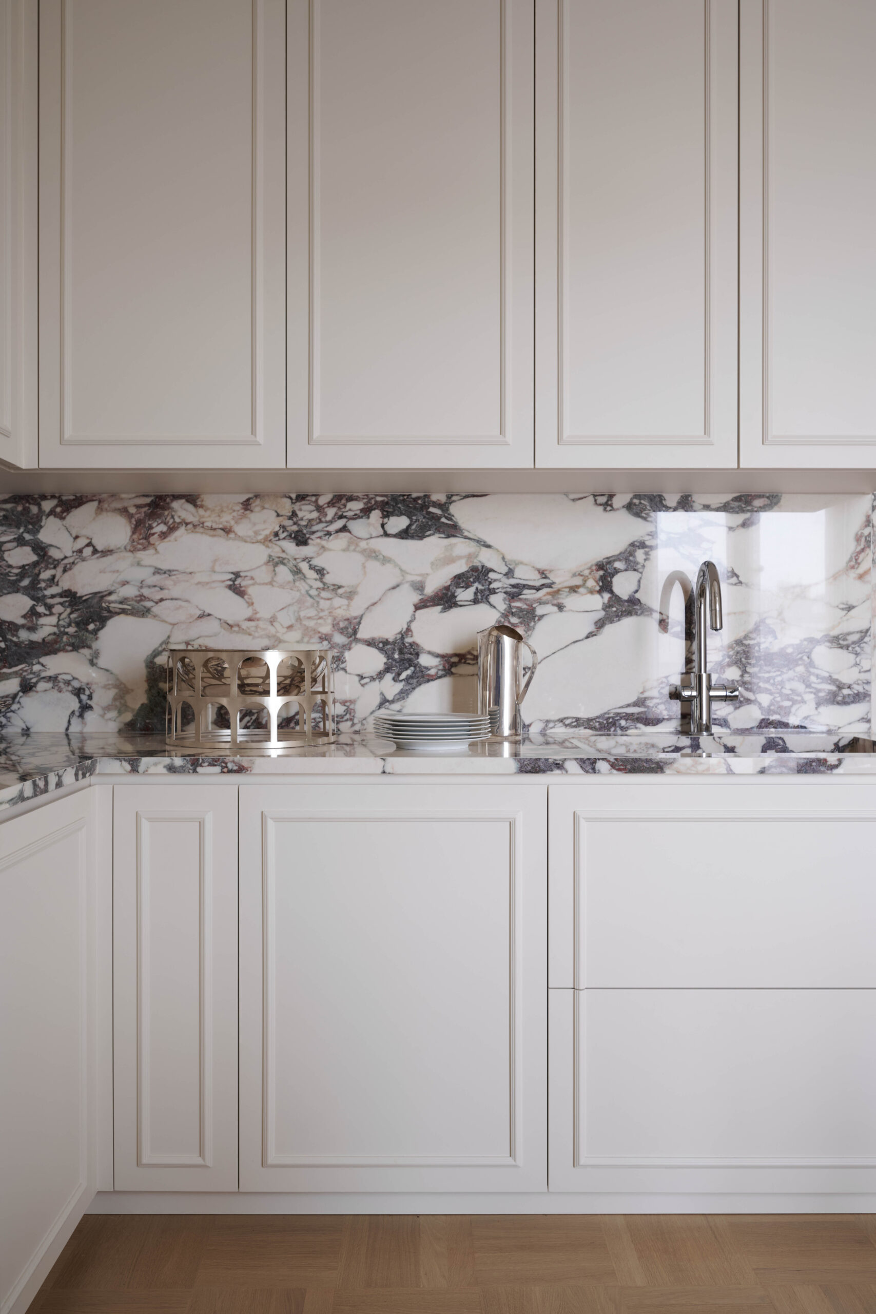 Cucina con ante color crema a cornice, piano e alzata in marmo bianco dalle venature scure, rubinetto cromato e oggetti metallici.