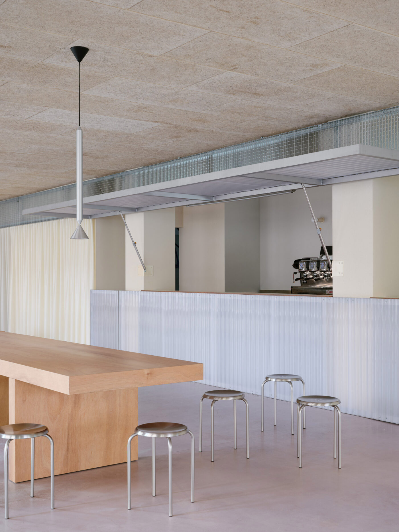 Bancone chiaro in policarbonato con sgabelli metallici, tavolo in legno e pavimento rosa.