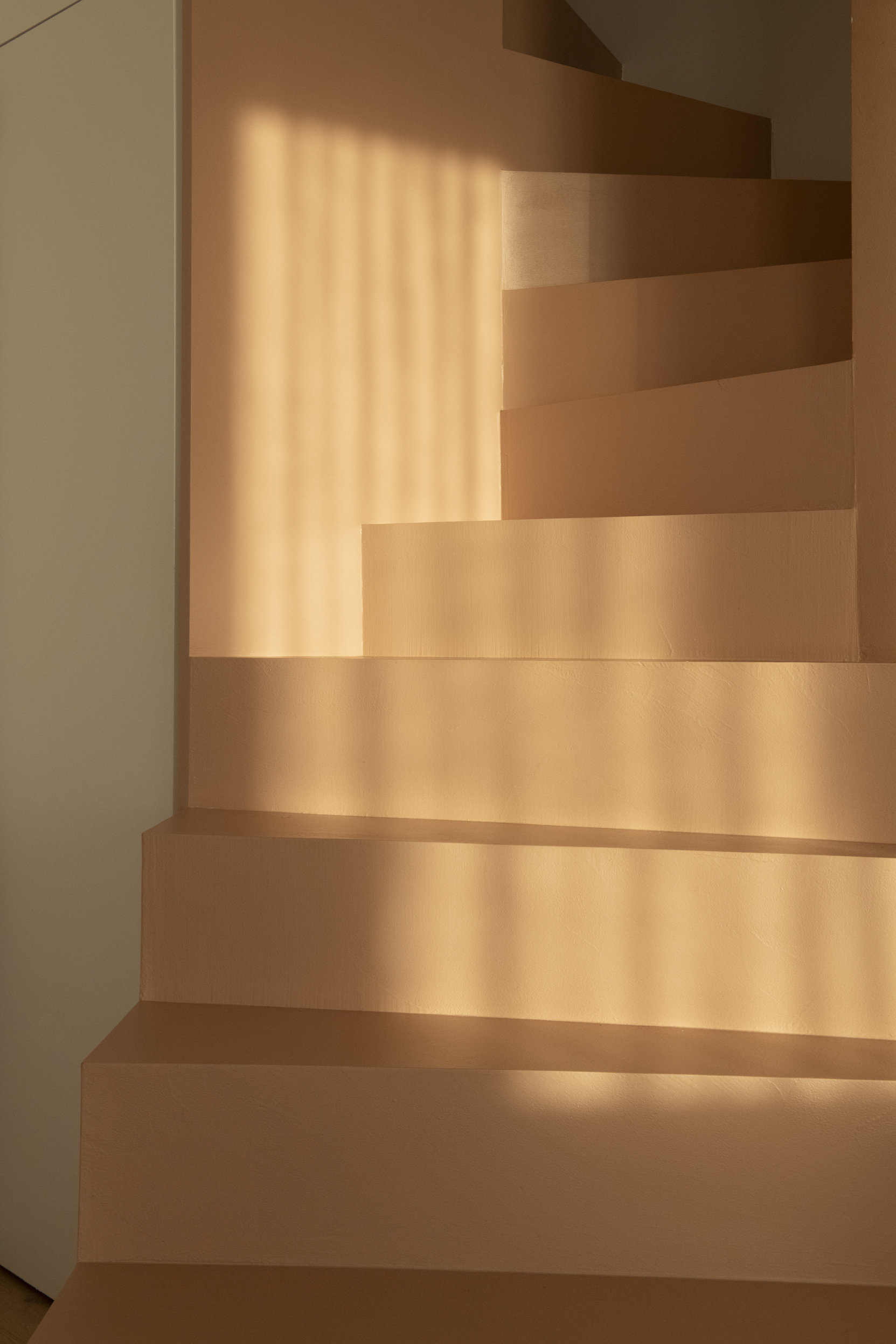 Dettaglio dei gradini color cipria attraversati da fasce di luce e ombra.