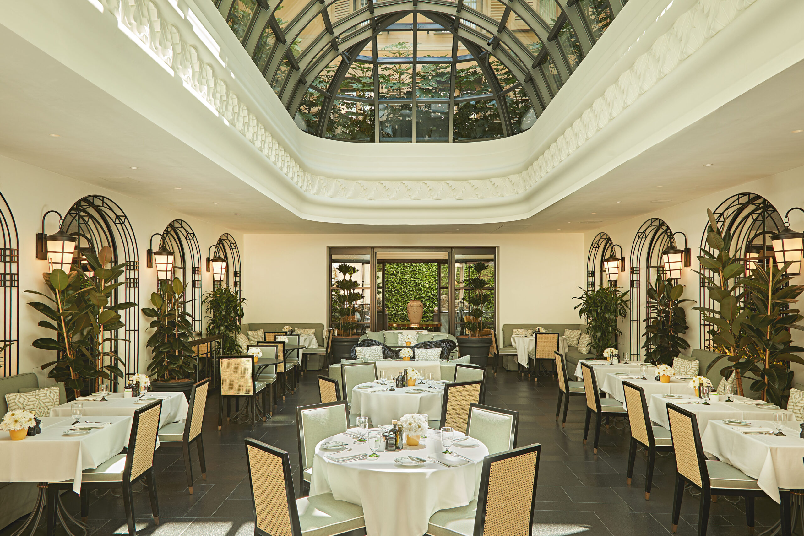 Cafe Floretta al The Carlton Milano, con cupola vetrata, specchi ad arco, piante e tavoli apparecchiati.