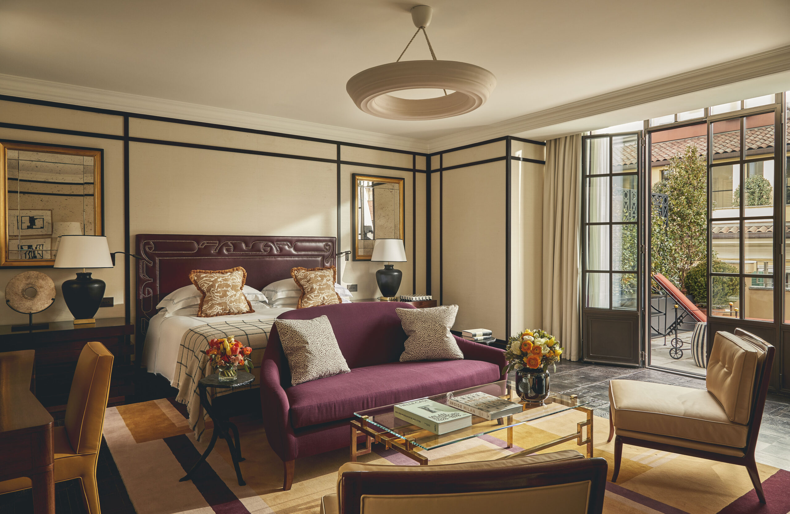 Presidential Suite con testata in pelle bordeaux, divano color prugna, tavolino in vetro e porte vetrate sul terrazzo.