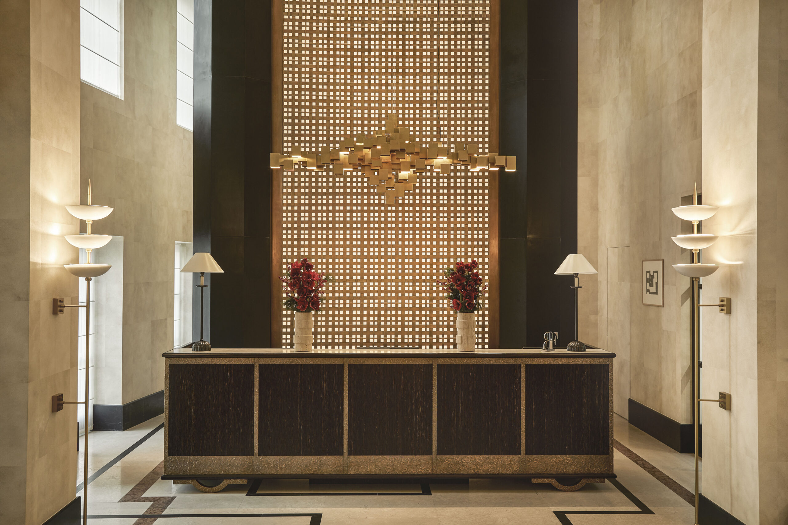 Reception del Carlton con banco scuro, pavimento geometrico, grande fondale traforato e lampade simmetriche.