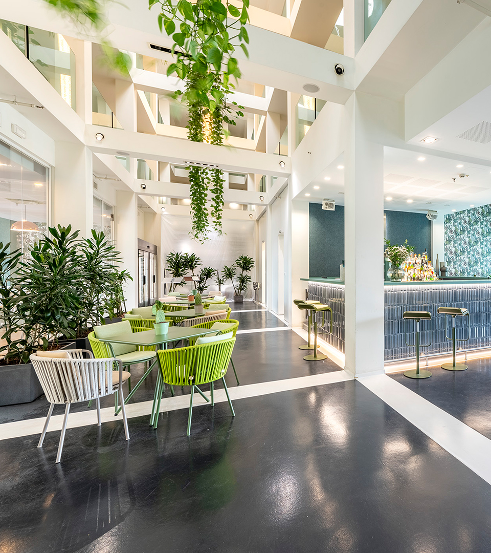 MO.OM Hotel atrium with a white structural grid, hanging plants, green chairs and a blue lounge bar.