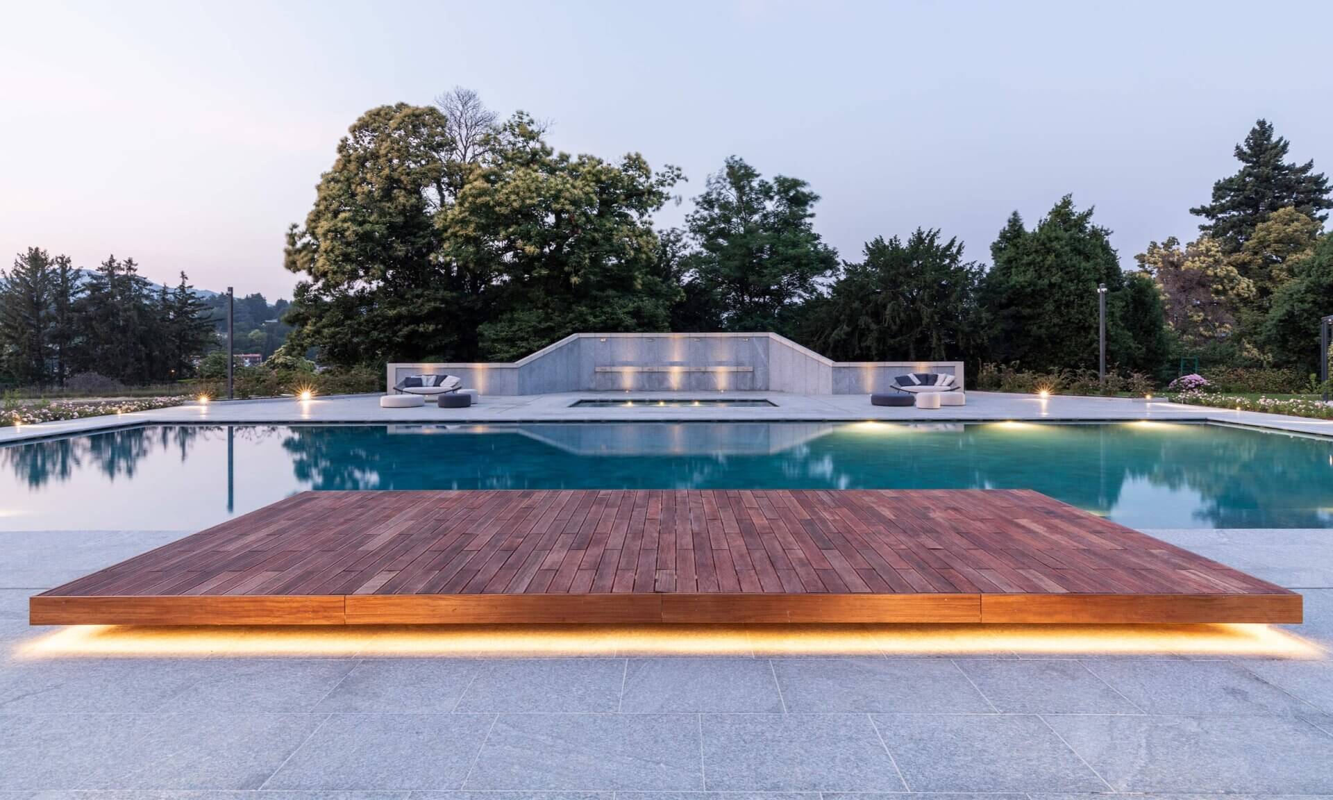 Palace Grand Hotel pool at dusk, with an illuminated timber platform and trees in the background.