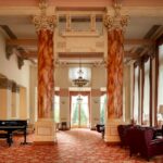 Salone del Palace Grand Hotel di Varese con colonne color ambra, capitelli decorati, pianoforte e divani bordeaux