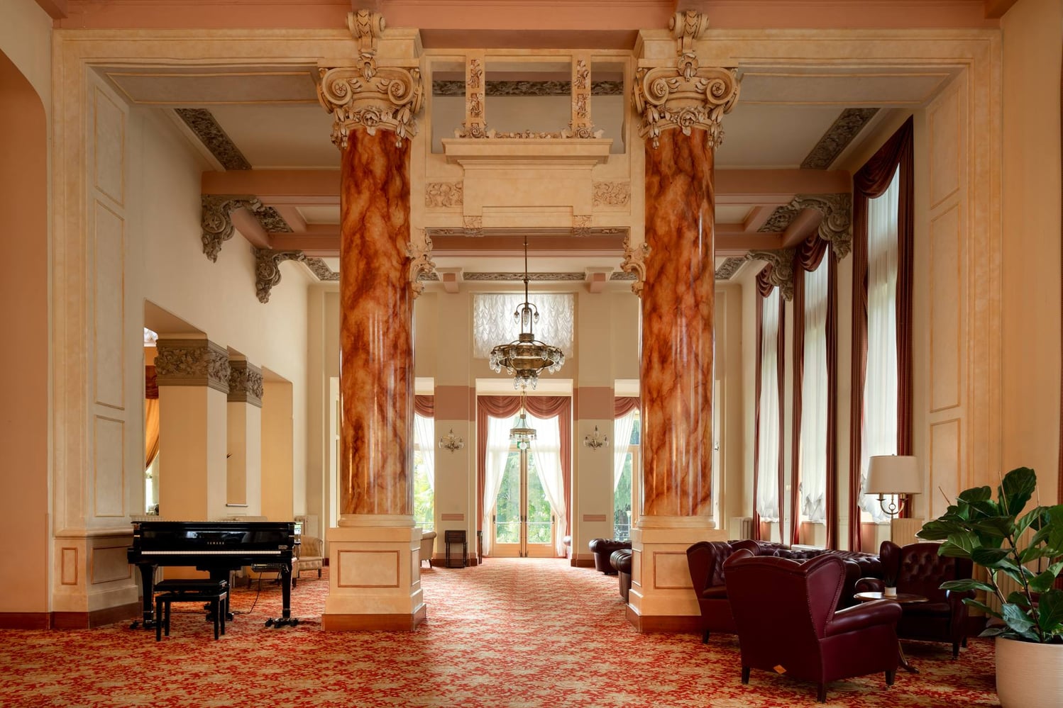 Salone del Palace Grand Hotel di Varese con colonne color ambra, capitelli decorati, pianoforte e divani bordeaux