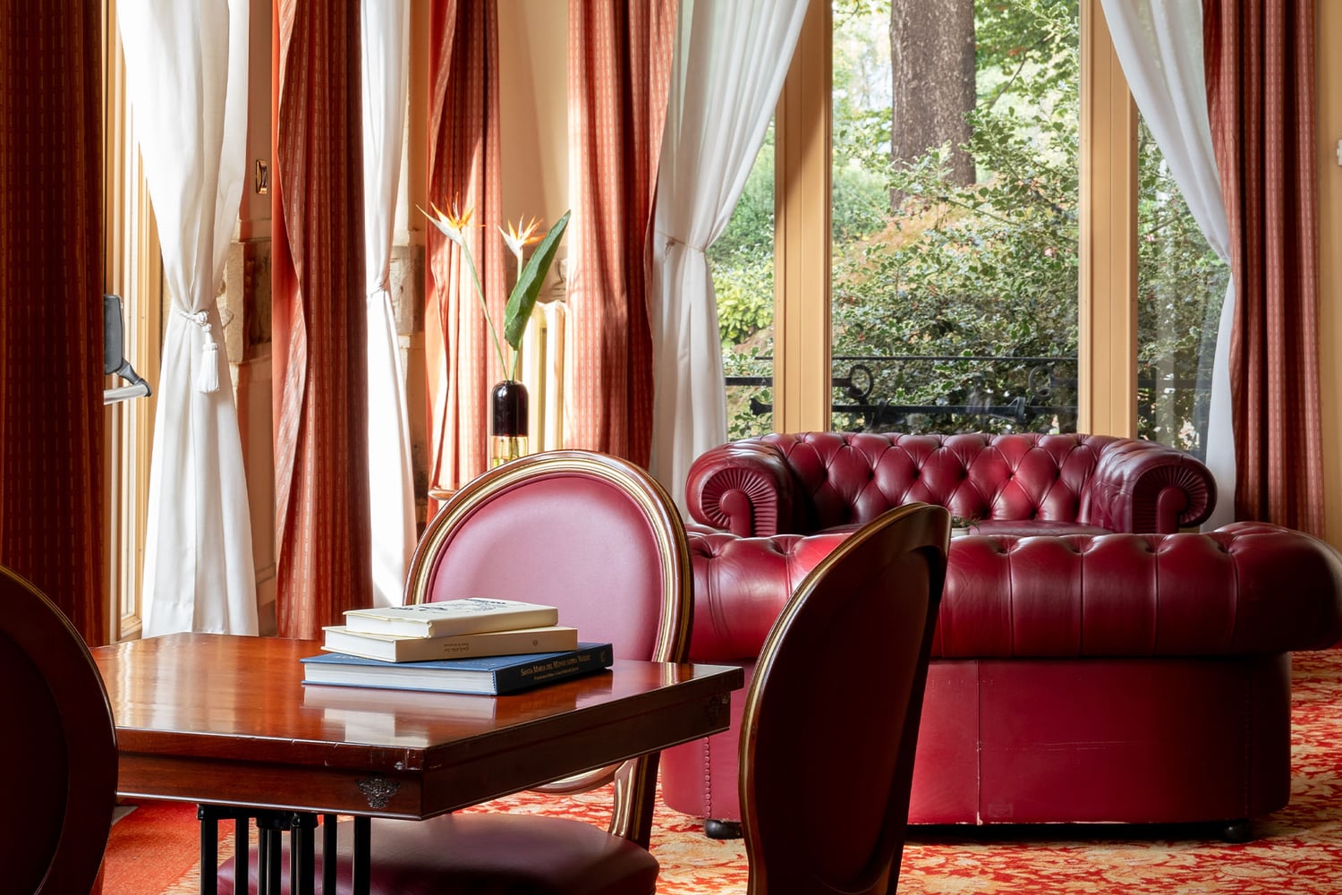Sitting room at Palace Grand Hotel with burgundy sofas, books on a table and windows overlooking the park.