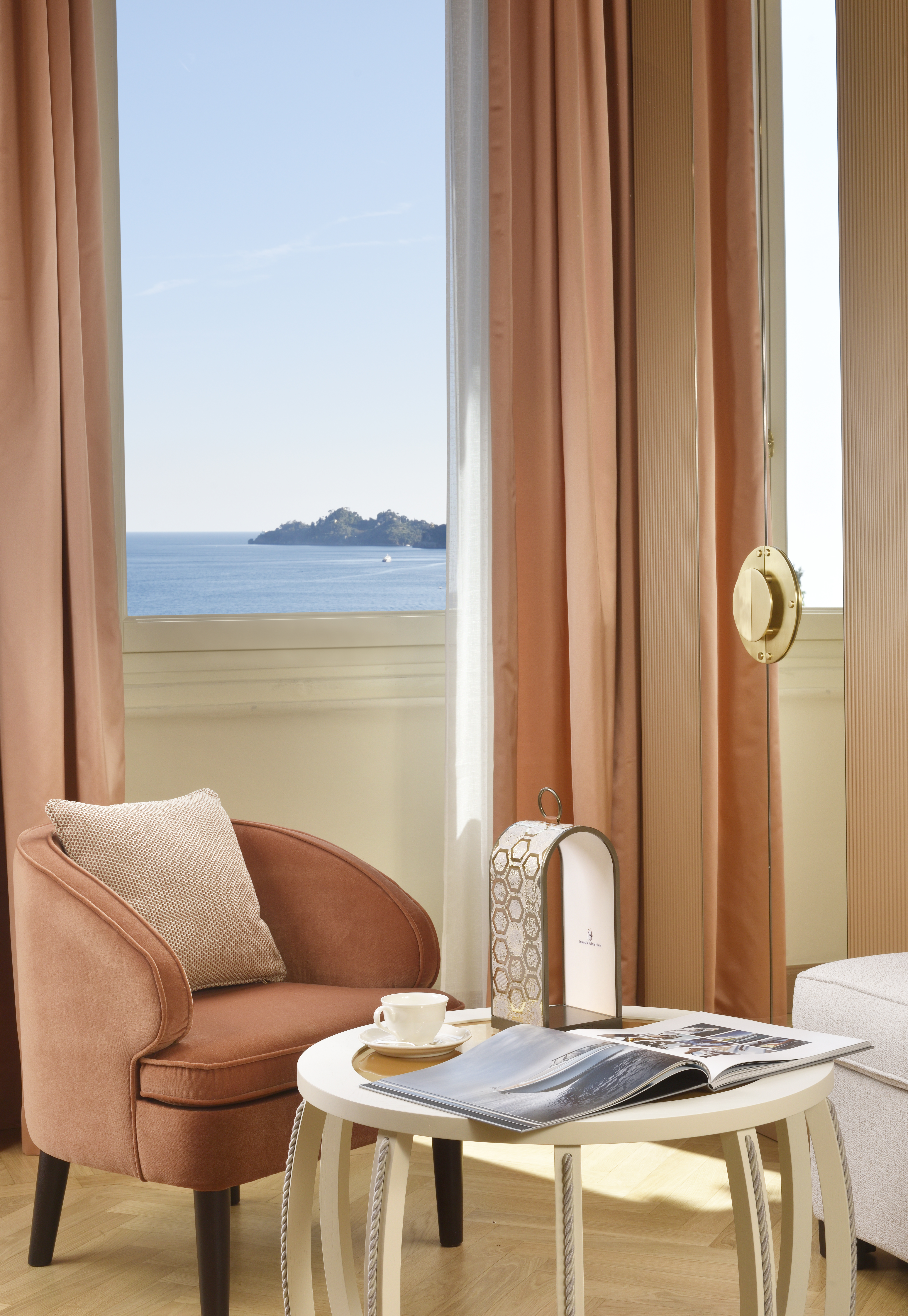 Dettaglio della Suite 219 con poltrona rosa, tavolino, finestra sul mare e particolare della maniglia in ottone.