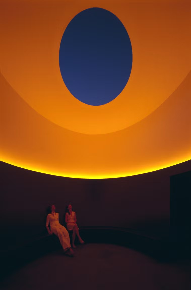 Interno di The Color Inside con soffitto arancione, apertura ovale sul cielo blu e visitatori seduti