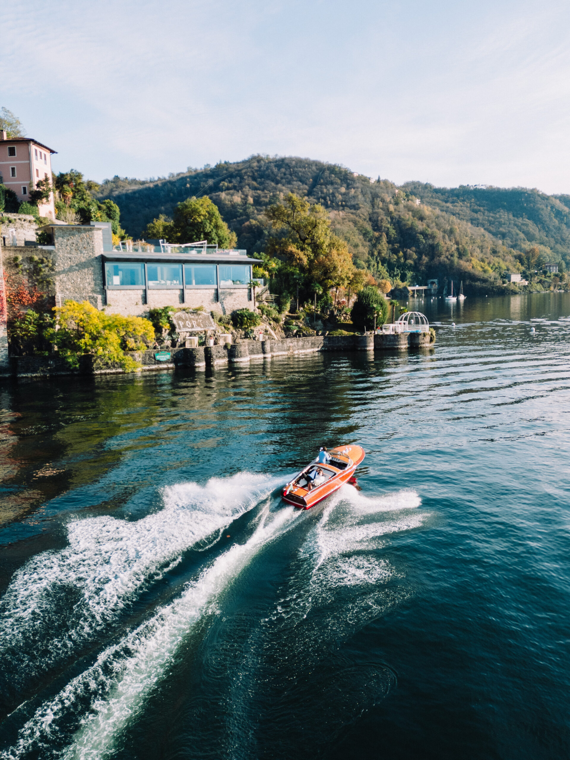 A Riva boat passing the gardens and waterfront buildings of Villa Porta in Colmegna.