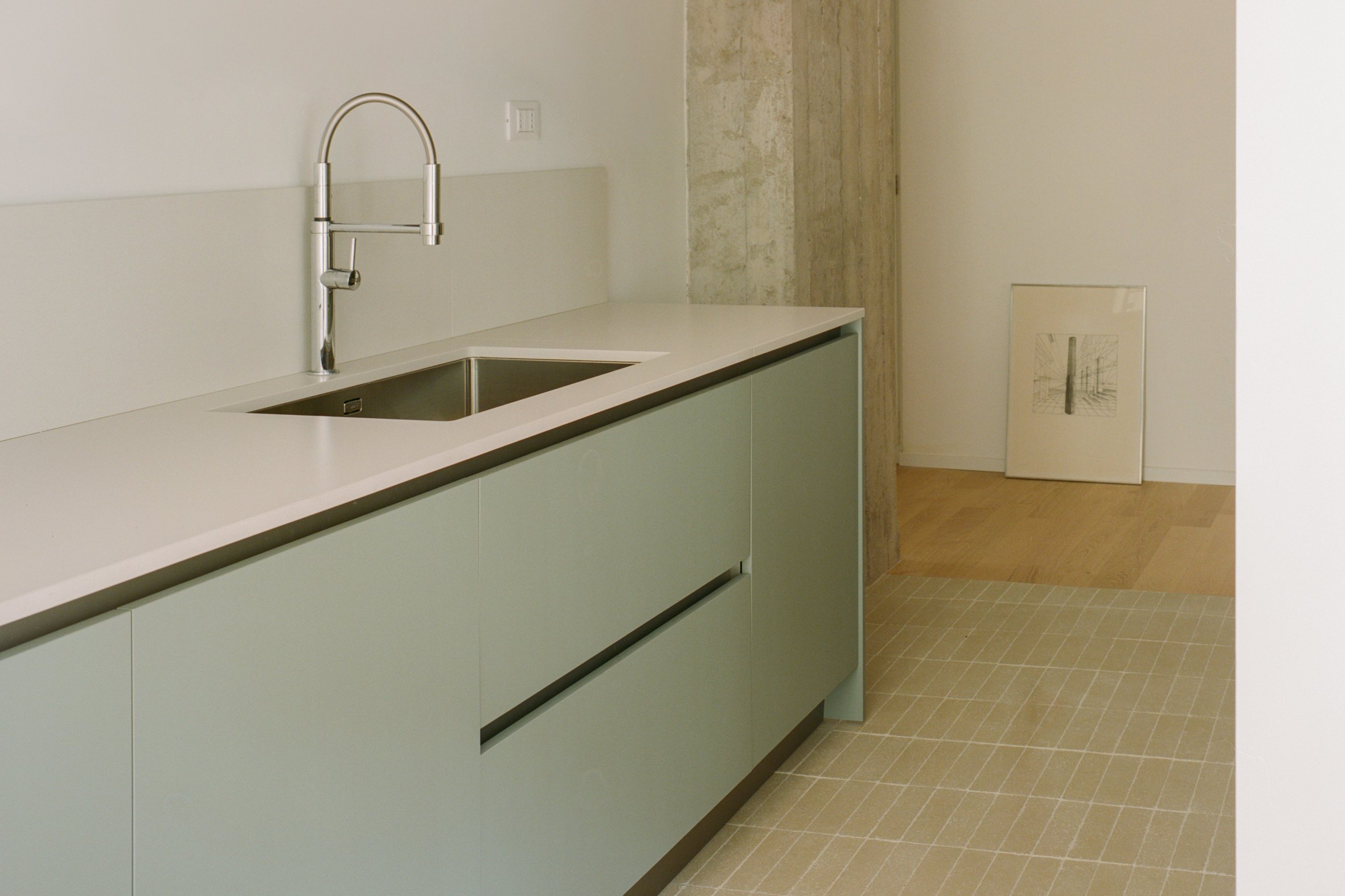 Cucina verde salvia con pilastro in cemento a vista nell’Apartment I di Atempora a Roma