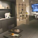 Showroom di arredamento a Milano con materioteca, campioni di finiture su mensole, tavolo da riunione e schermo con render di progetto