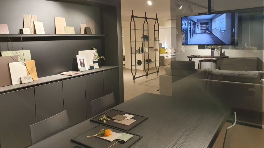 Showroom di arredamento a Milano con materioteca, campioni di finiture su mensole, tavolo da riunione e schermo con render di progetto