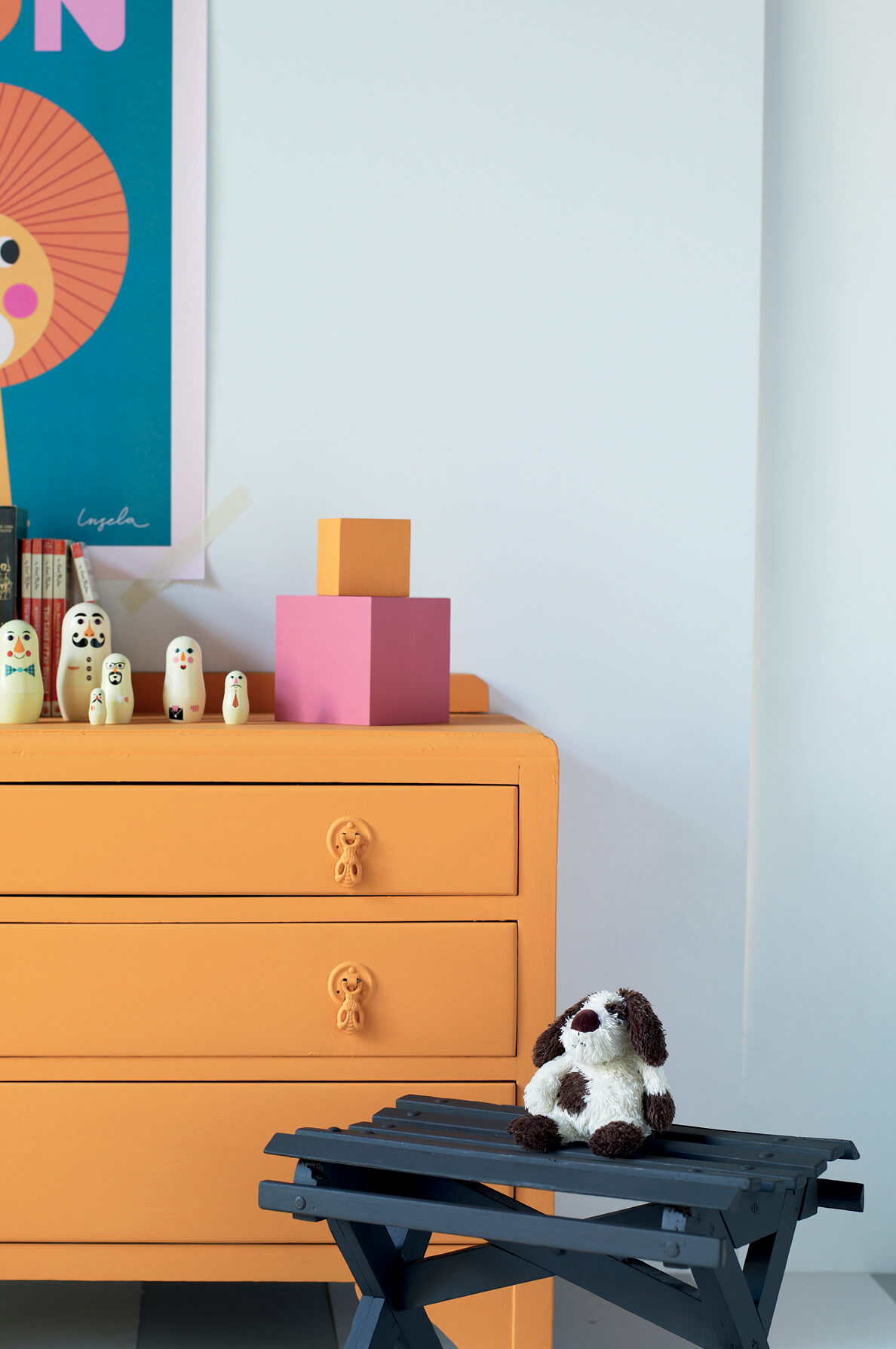 Children's room with a pale blue-grey wall, an orange chest of drawers and a dark blue bench