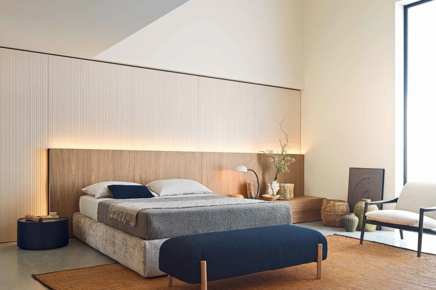 Double bedroom with illuminated wooden headboard, blue bench and natural fibre rug