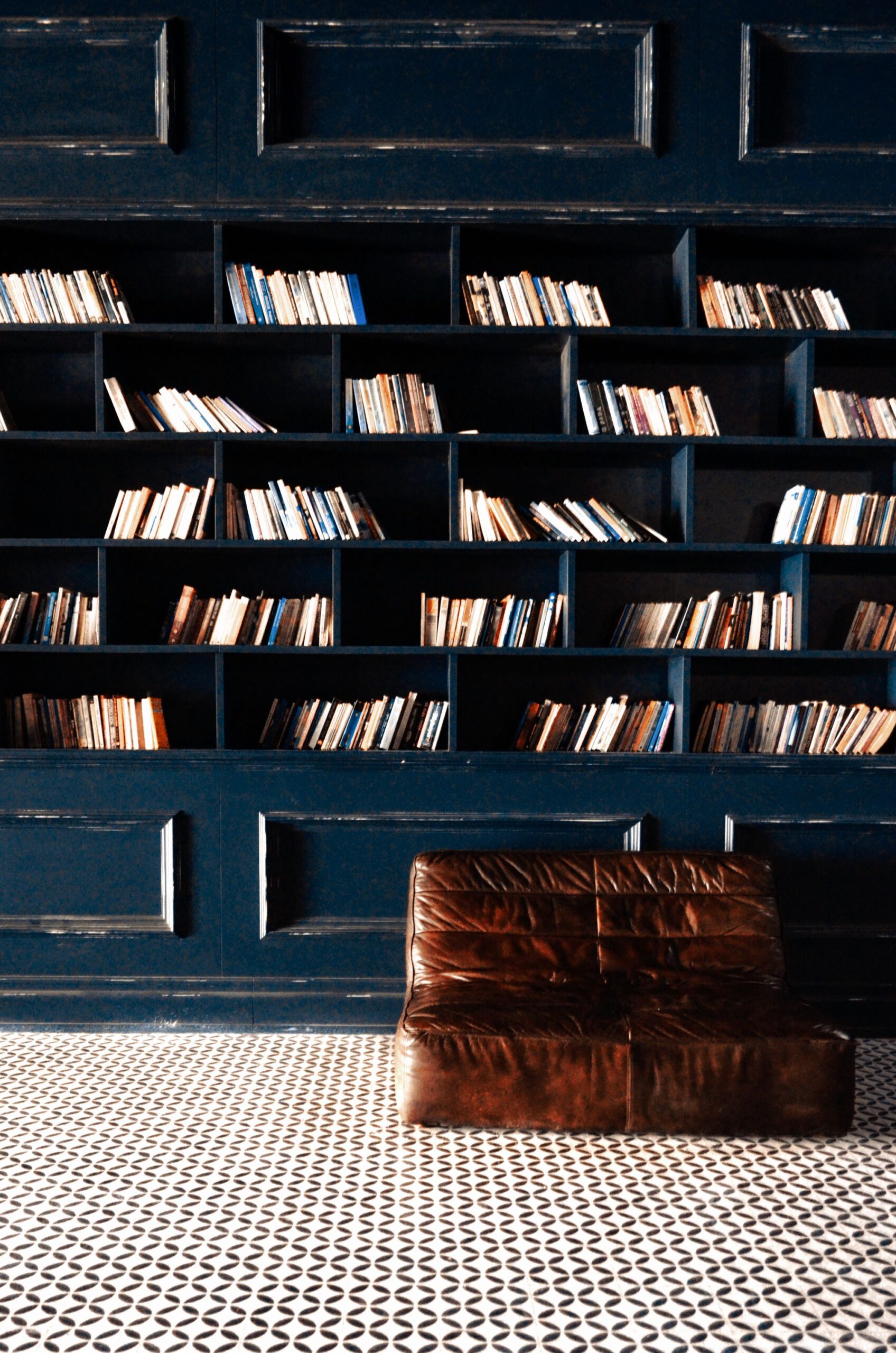 Libreria dalle pareti blu con divano in pelle marrone