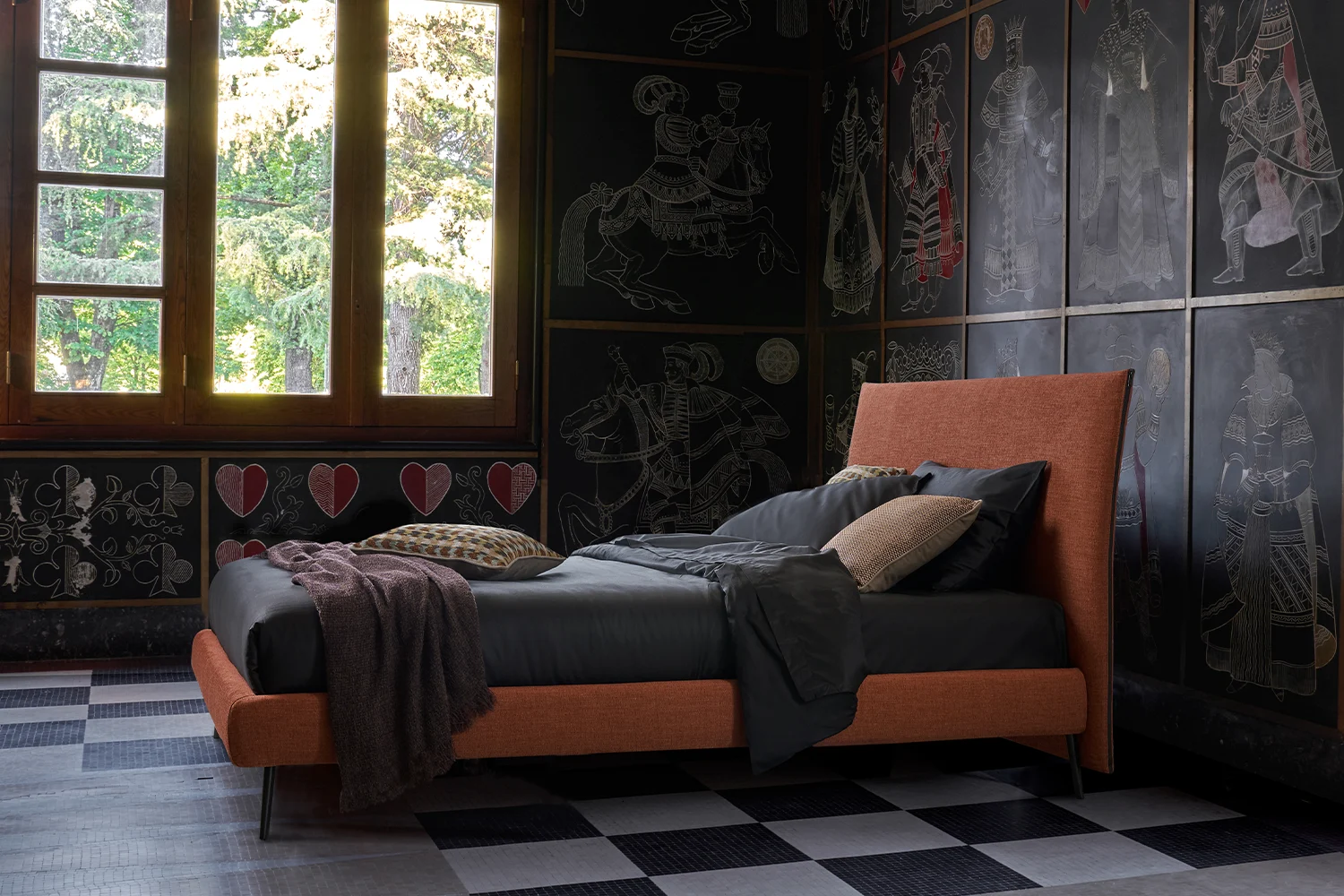 Orange upholstered bed with grey and rust bedding in a room with dark decorated walls and a chequered floor