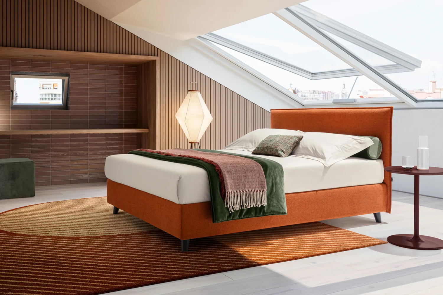 Attic bedroom with an orange upholstered bed under a roof window, a rug with curved patterns and a paper lamp