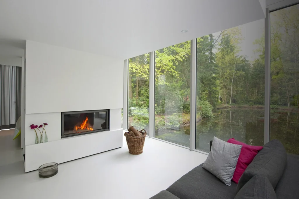 Modern wood-burning fireplace with a panoramic flush flame in a living room overlooking woodland