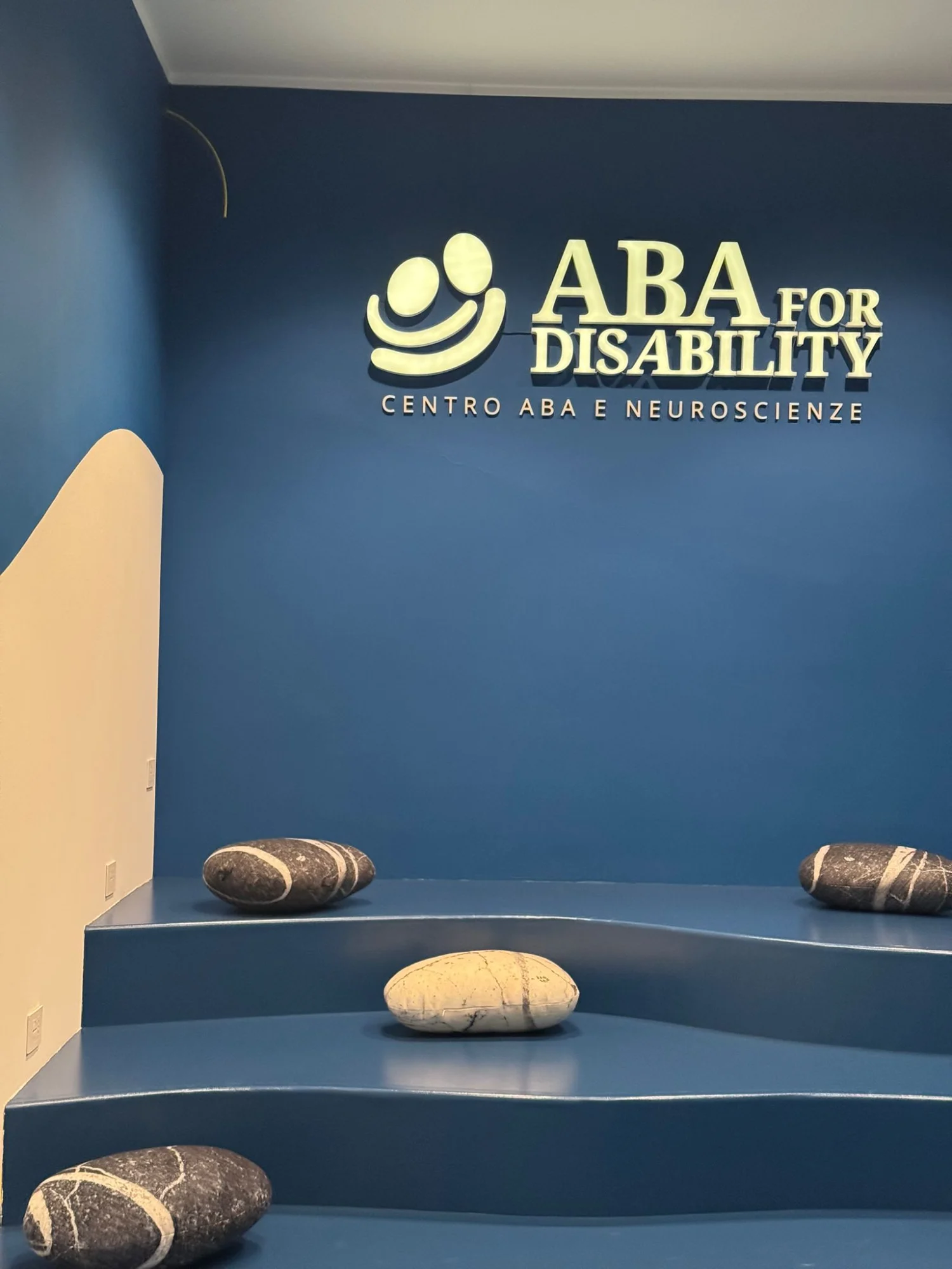 Sala del Centro ABA for Disability di Salerno con parete blu, onda color sabbia e gradoni con sedute a forma di sasso