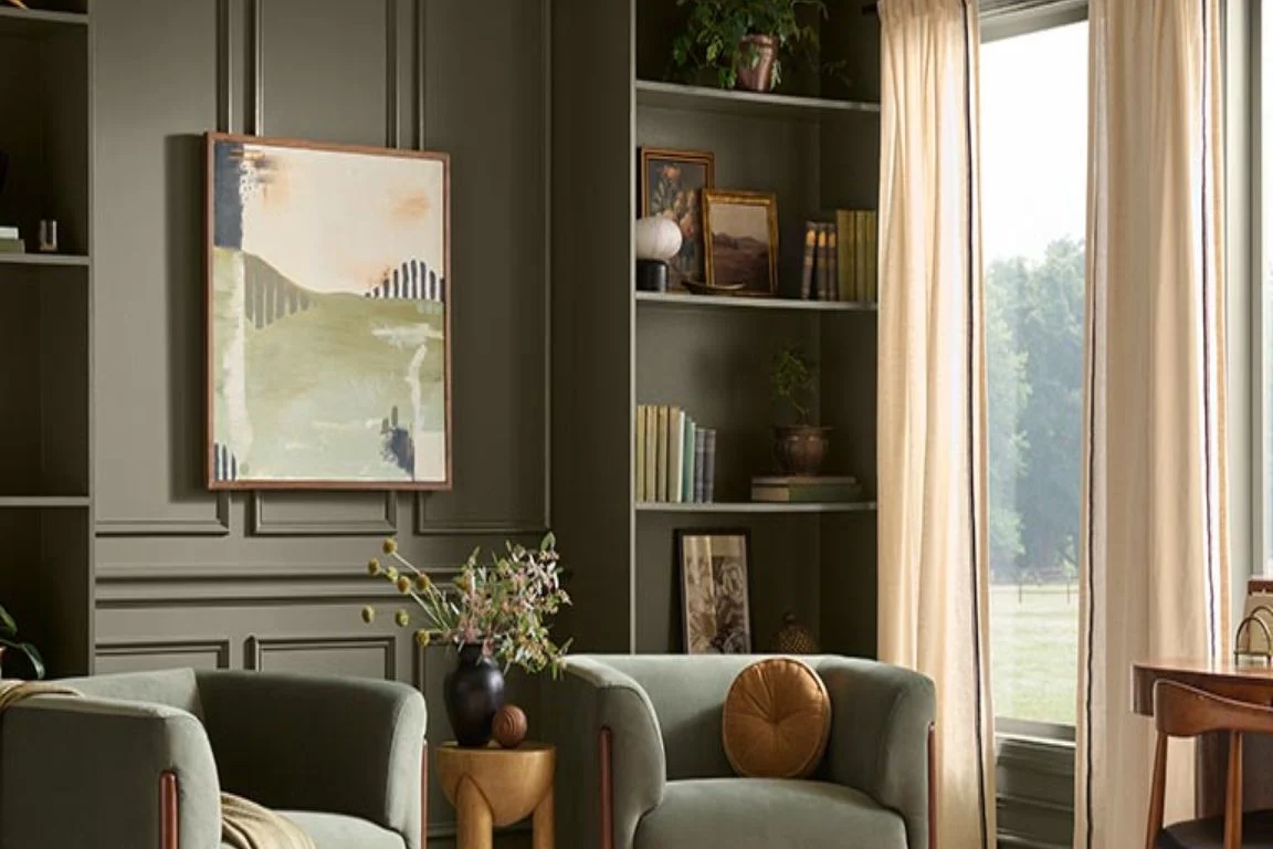 Living room with dark olive green walls and shelving and velvet armchairs