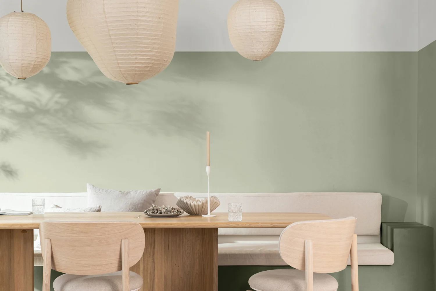 Sala da pranzo con pareti verde salvia, tavolo in legno chiaro e lampade in carta