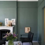 Soggiorno con pareti verde grigio, camino e poltrona in pelle nera