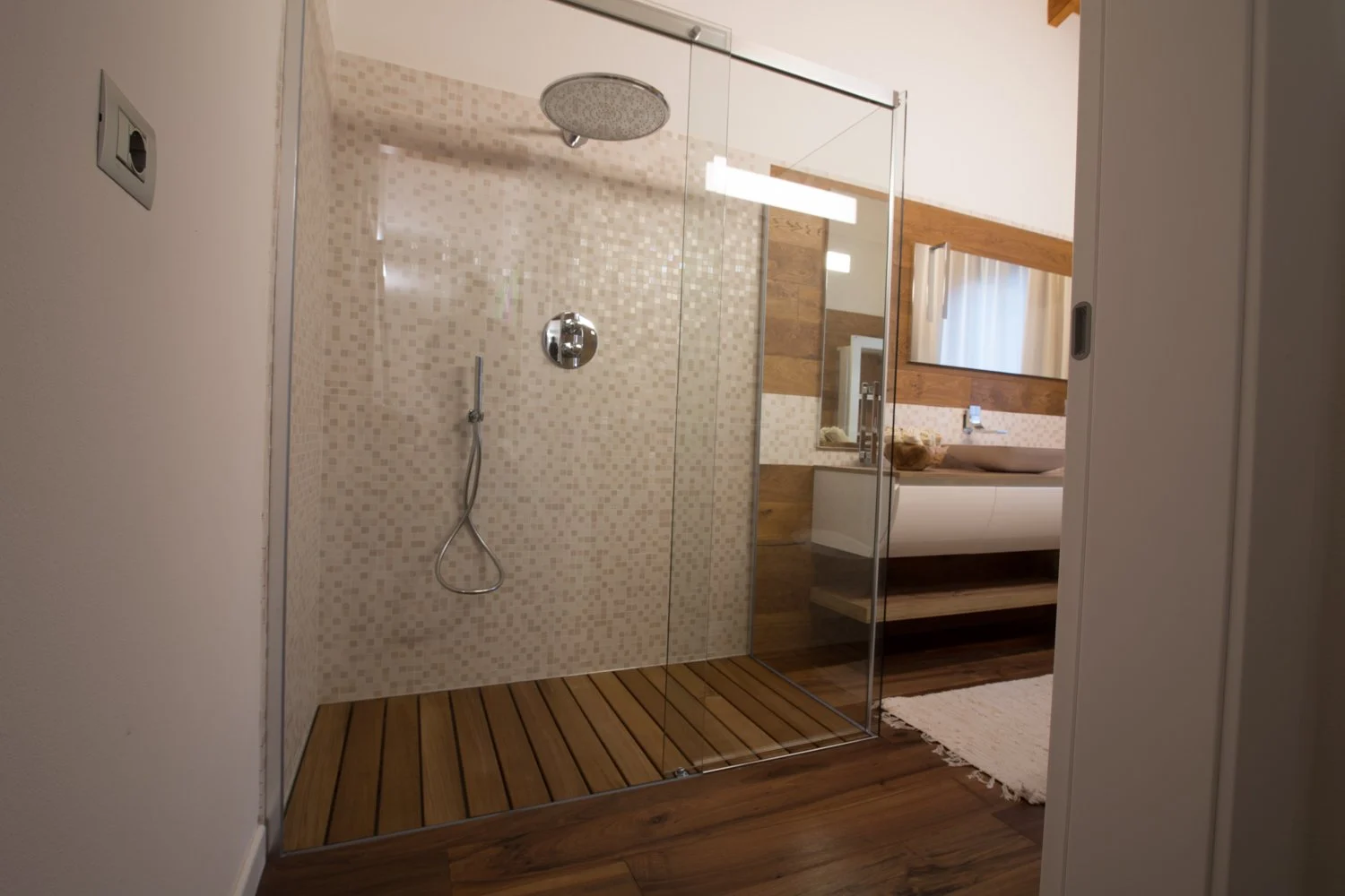 Doccia walk in a filo pavimento con pedana in doghe di legno, vetro trasparente e soffione a soffitto