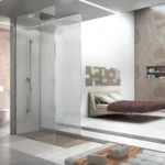 Doccia walk in con due lastre di vetro senza profili e soffione a soffitto in un bagno aperto sulla camera