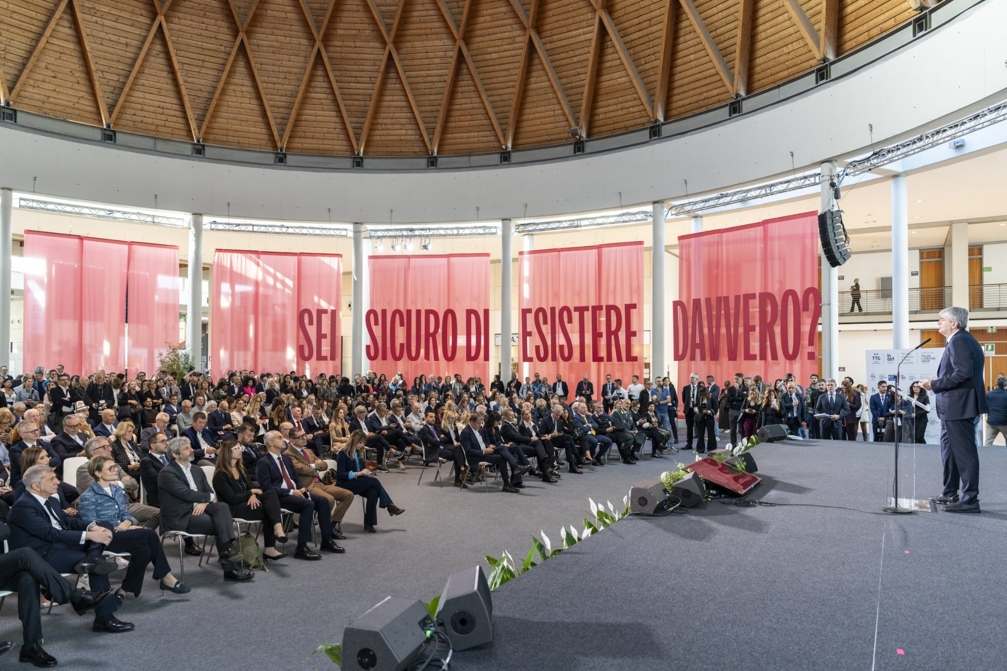 Platea dell’Opening Ceremony di TTG e InOut 2026 alla Fiera di Rimini, con la scritta “Sei sicuro di esistere davvero?” del tema Exist