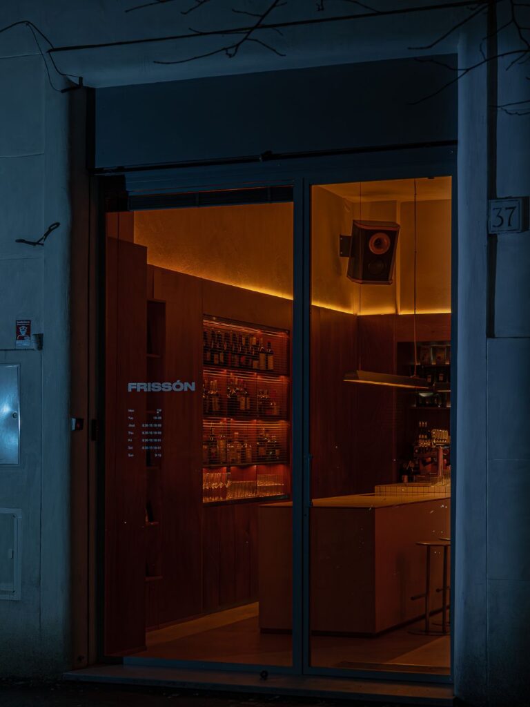 Ingresso notturno di Frissón a Roma con vetrina illuminata e interni in legno caldo