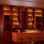 Parete di vinili retroilluminata con due diffusori hi-fi integrati e consolle sotto pannelli acustici sospesi da Frissón a Roma